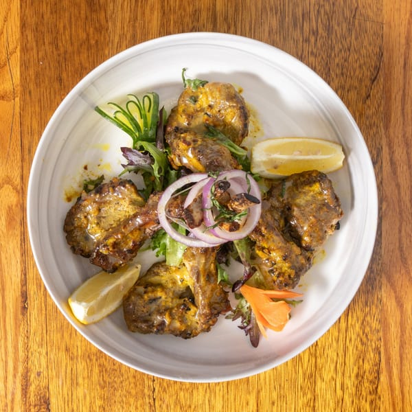 Grilled lamb chops with lemon wedges, red onion, and green garnish on a white plate.