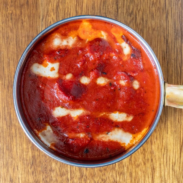 Overhead view of a metal pan filled with red sauce and white creamy swirls on a wooden table.