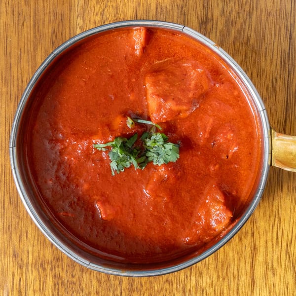 Overhead view of a metal bowl filled with vibrant red curry, garnished with fresh cilantro.