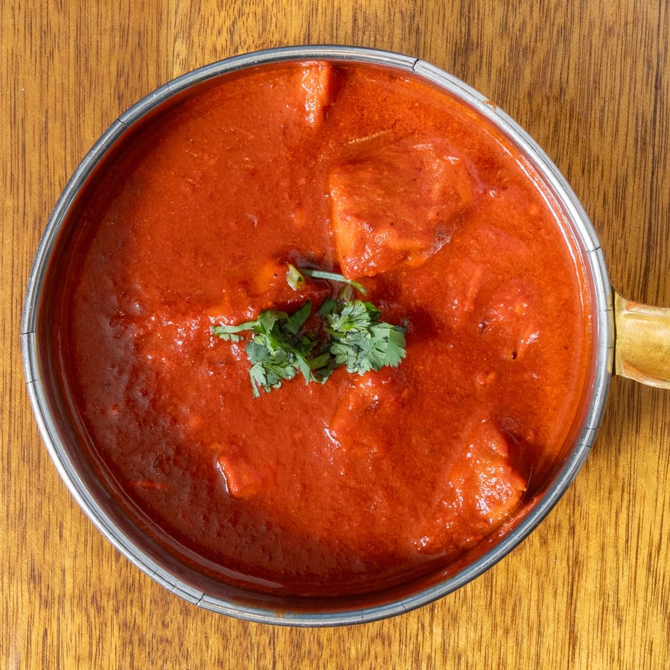 Overhead view of a metal bowl filled with vibrant red curry, garnished with fresh cilantro.
