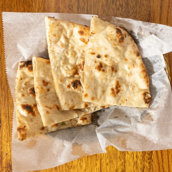 Golden brown naan bread pieces, lightly charred, served in a basket lined with white parchment paper.