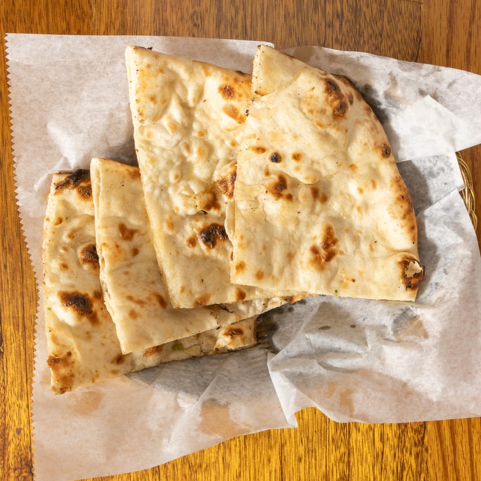 Golden brown naan bread pieces, lightly charred, served in a basket lined with white parchment paper.