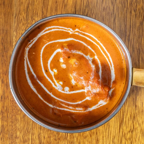 Overhead view of a metal bowl filled with orange curry, swirled with white cream.