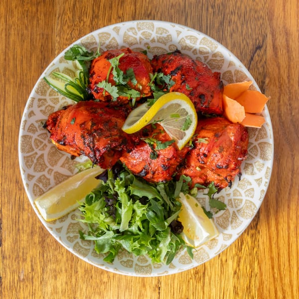 Tandoori chicken with fresh cilantro, lemon wedges, and a side salad on a patterned plate.