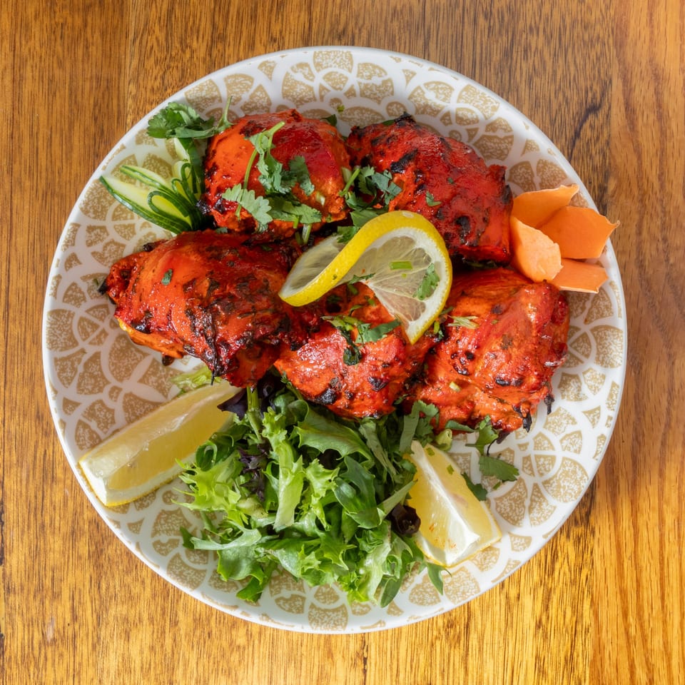 Tandoori chicken with fresh cilantro, lemon wedges, and a side salad on a patterned plate.
