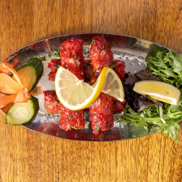 Red marinated meat skewers with lemon slices, cucumber, carrots, and lettuce on a silver platter.