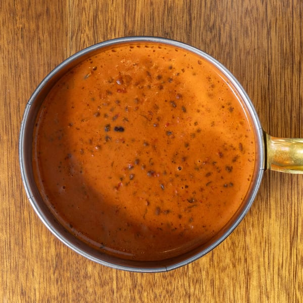 Overhead view of a small metal pot filled with orange-brown Indian dal on a wooden table.