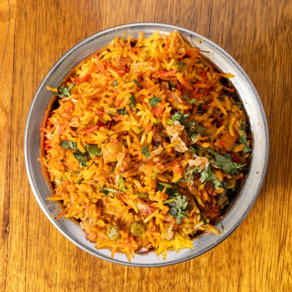 A metal bowl filled with vibrant orange and yellow biryani rice, garnished with fresh cilantro.